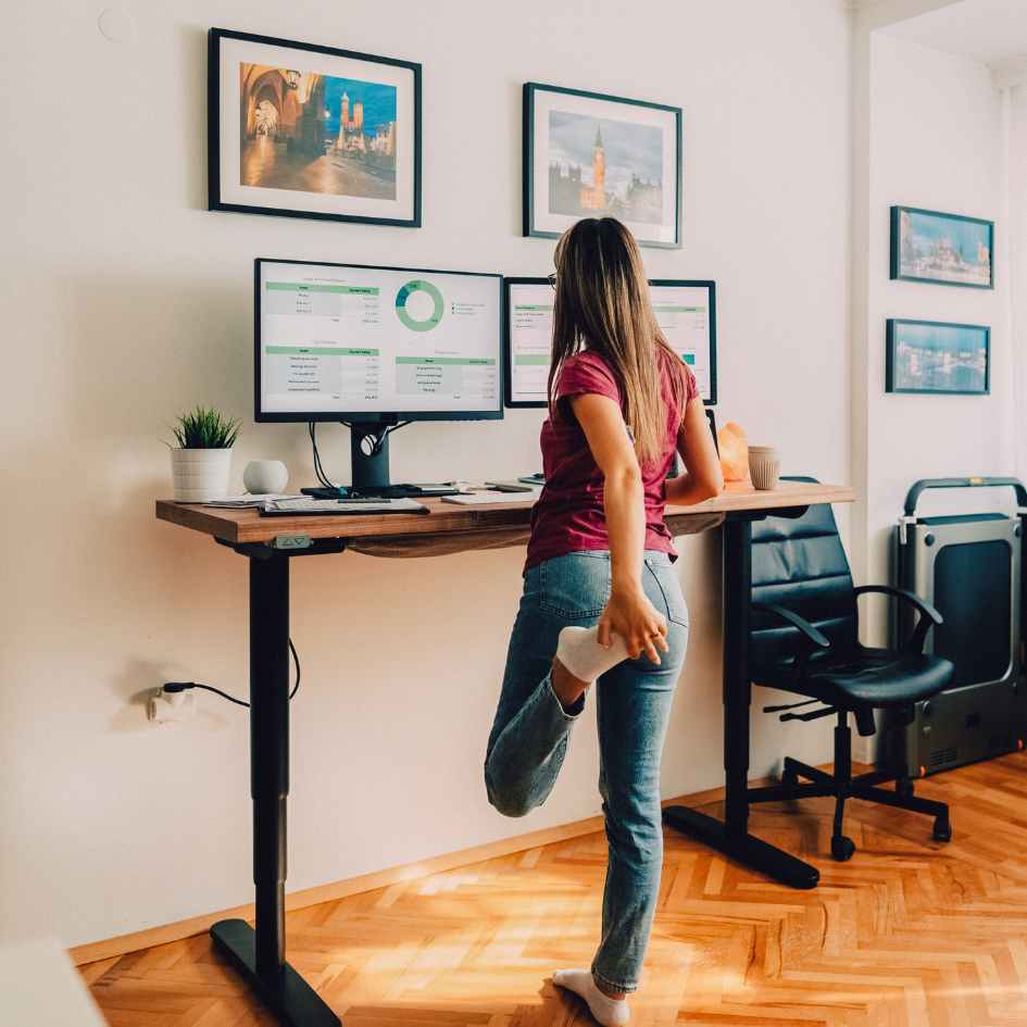Women standing stretching leg whilst working from home at her ergonomic desk from Pure Office Solutions